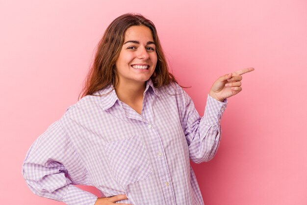 Young caucasian woman isolated on pink background  smiling cheerfully pointing with forefinger away.