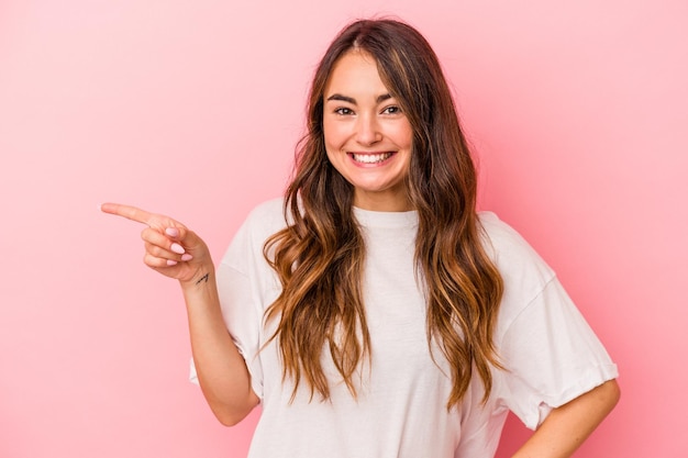 Young caucasian woman isolated on pink background smiling cheerfully pointing with forefinger away.