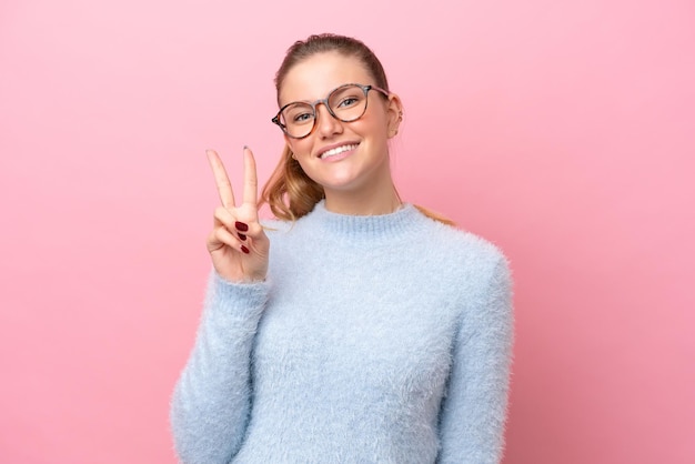 Young caucasian woman isolated on pink background smiling and showing victory sign