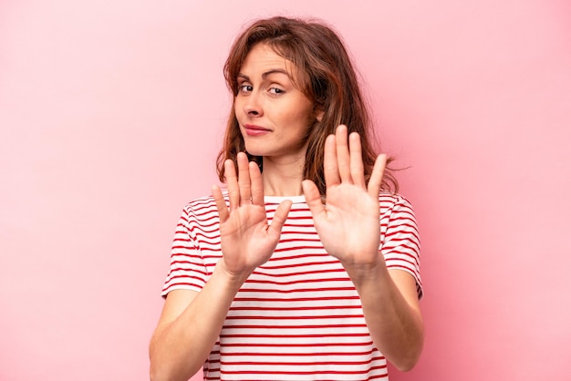 Young caucasian woman isolated on pink background standing with outstretched hand showing stop sign preventing you