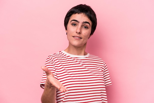 Young caucasian woman isolated on pink background stretching hand at camera in greeting gesture.