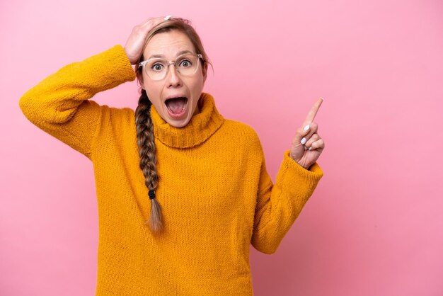 Young caucasian woman isolated on pink background surprised and pointing finger to the side