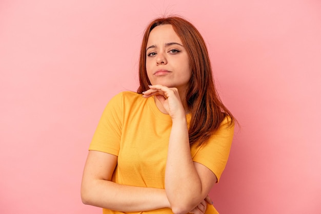 Young caucasian woman isolated on pink background suspicious, uncertain, examining you.