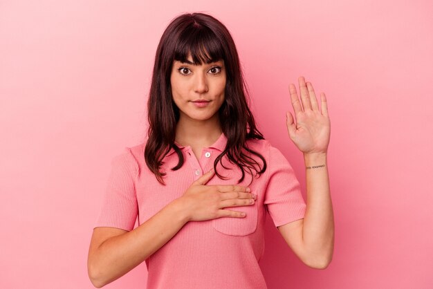 Young caucasian woman isolated on pink background taking an oath, putting hand on chest.