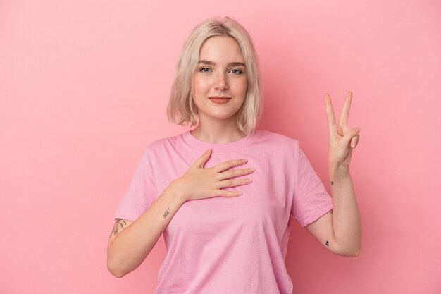 Young caucasian woman isolated on pink background taking an oath, putting hand on chest.