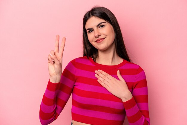 Young caucasian woman isolated on pink background taking an oath putting hand on chest