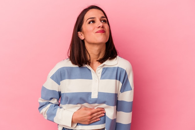 Young caucasian woman isolated on pink background touches tummy, smiles gently, eating and satisfaction concept.