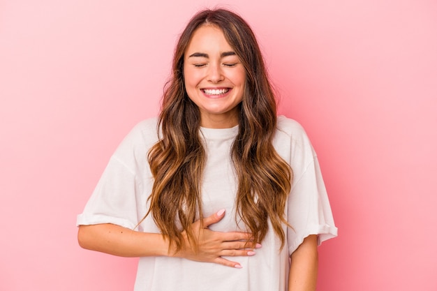 Young caucasian woman isolated on pink background touches tummy, smiles gently, eating and satisfaction concept.