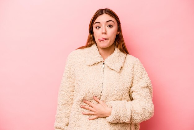 Young caucasian woman isolated on pink background touches tummy smiles gently eating and satisfaction concept