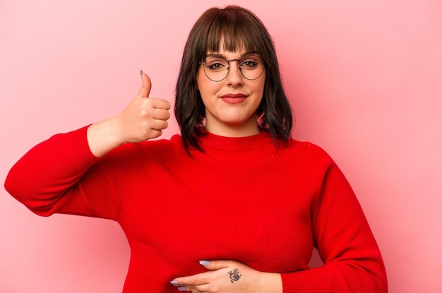 Young caucasian woman isolated on pink background touches tummy smiles gently eating and satisfaction concept