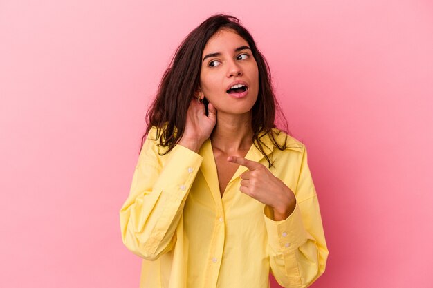 Young caucasian woman isolated on pink background trying to listening a gossip.