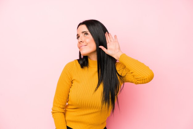 Young caucasian woman isolated on pink background trying to listening a gossip.