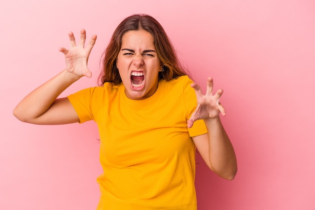 Young caucasian woman isolated on pink background  upset screaming with tense hands.