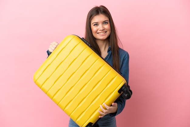Young caucasian woman isolated on pink background in vacation with travel suitcase