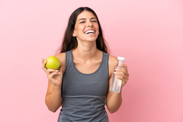 Young caucasian woman isolated on pink background with an apple and with a bottle of water