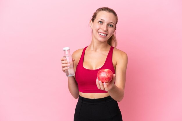 Young caucasian woman isolated on pink background with an apple and with a bottle of water