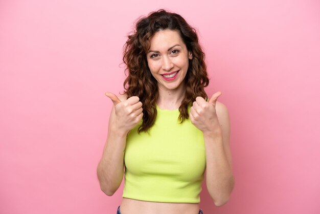 Young caucasian woman isolated on pink background with thumbs up gesture and smiling