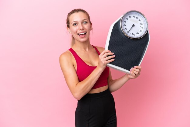 Young caucasian woman isolated on pink background with weighing machine