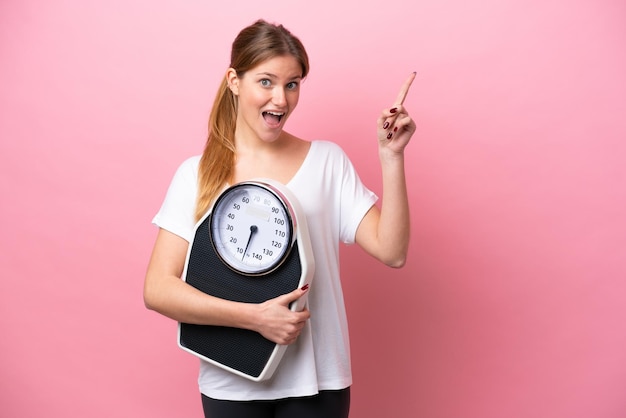 Young caucasian woman isolated on pink background with weighing machine