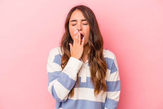 Young caucasian woman isolated on pink background yawning showing a tired gesture covering mouth with hand.