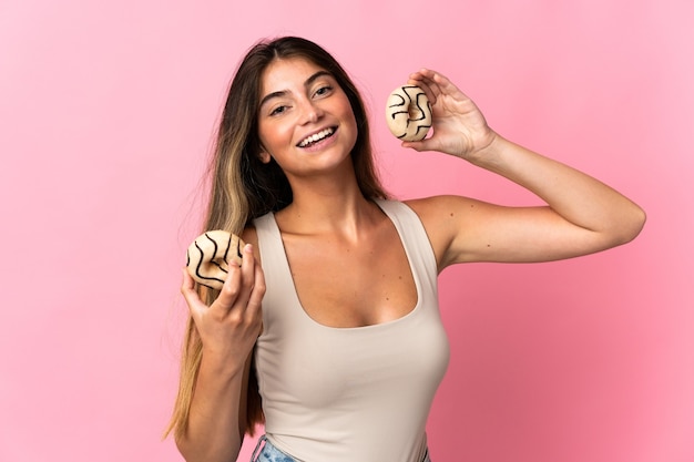 Young caucasian woman isolated on pink holding a donut and happy