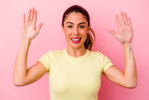 Young caucasian woman isolated on pink holding something little with forefingers, smiling and confident.