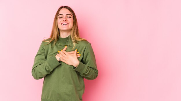 Young caucasian woman isolated on pink laughing keeping hands on heart, concept of happiness.