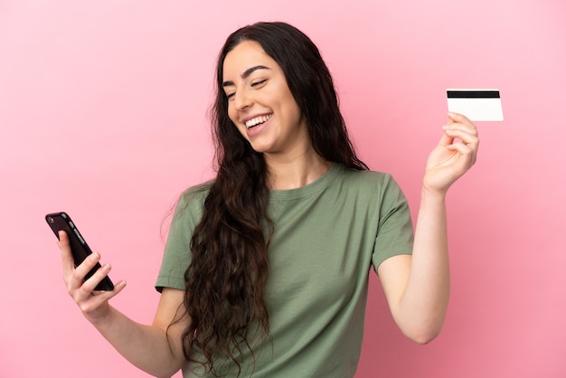 Young caucasian woman isolated on pink wall buying with the mobile with a credit card