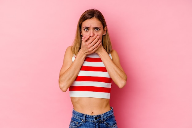 Young caucasian woman isolated on pink wall covering mouth with hands looking worried.