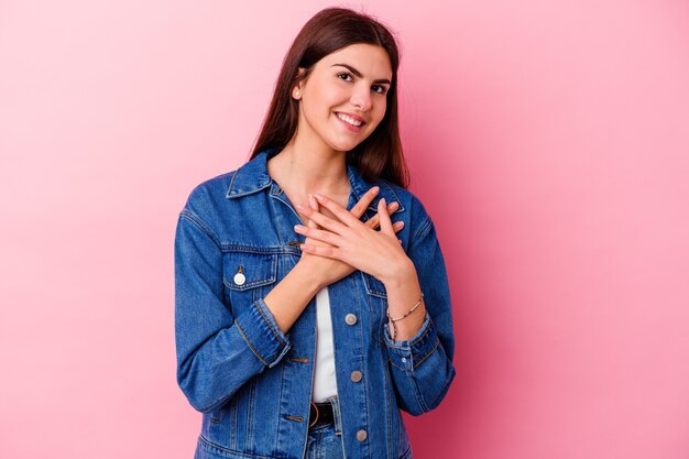 Young caucasian woman isolated on pink wall has friendly expression, pressing palm to chest. Love concept.