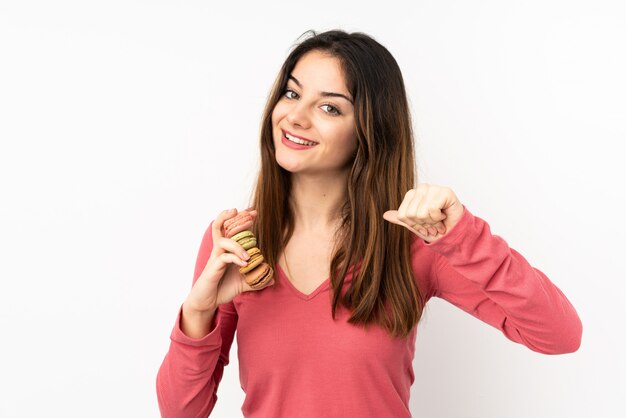 Young caucasian woman isolated on pink wall holding colorful French macarons and proud