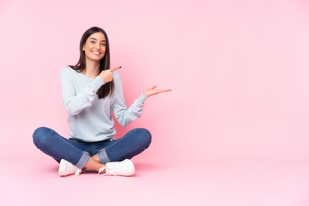 Young caucasian woman isolated on pink wall holding copyspace imaginary on the palm to insert an ad