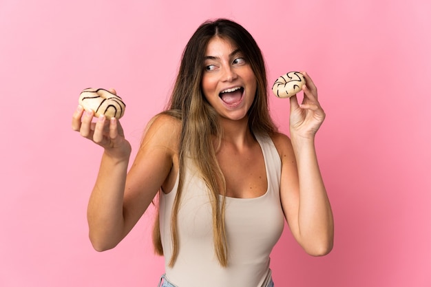 Young caucasian woman isolated on pink wall holding donuts with happy expression