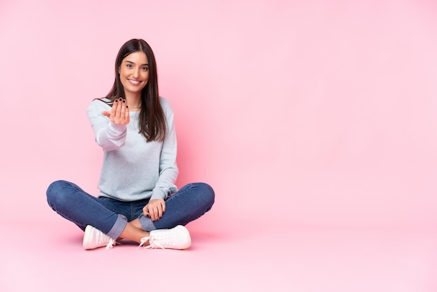 Young caucasian woman isolated on pink wall inviting to come with hand. Happy that you came