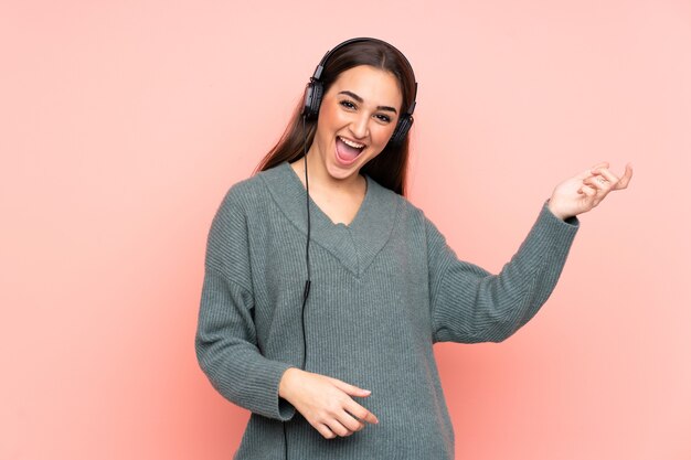 Young caucasian woman isolated on pink wall listening music and doing guitar gesture