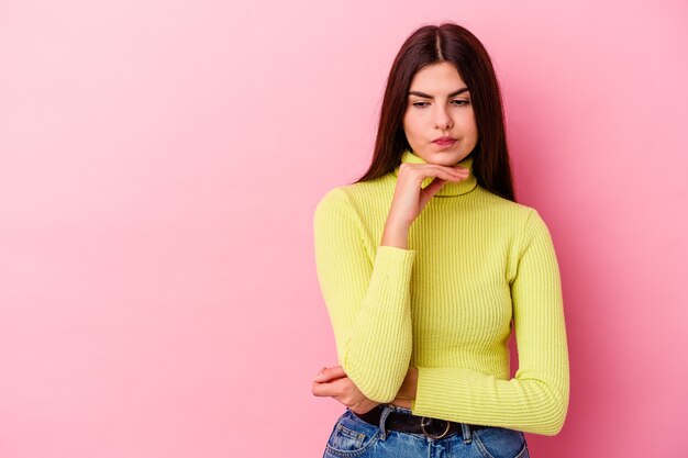 Young caucasian woman isolated on pink wall looking sideways with doubtful and skeptical expression.