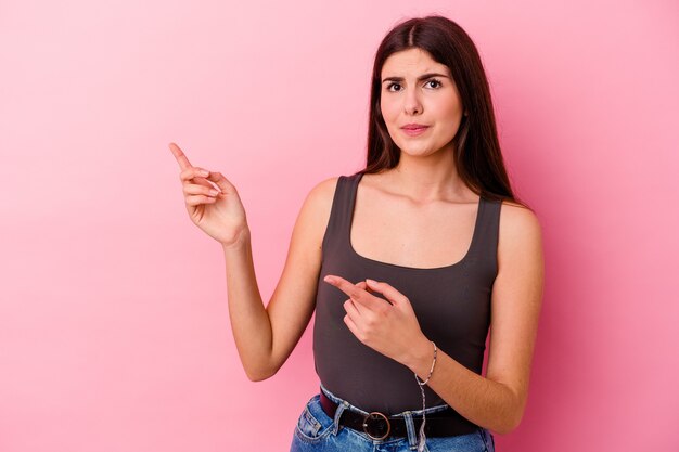 Giovane donna caucasica isolata sulla parete rosa scioccata che punta con il dito indice a uno spazio di copia.