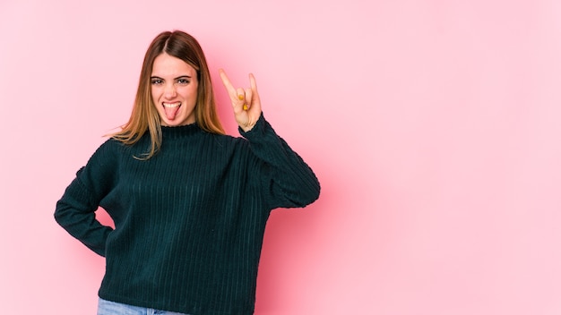 Young caucasian woman isolated on pink wall showing rock gesture with fingers