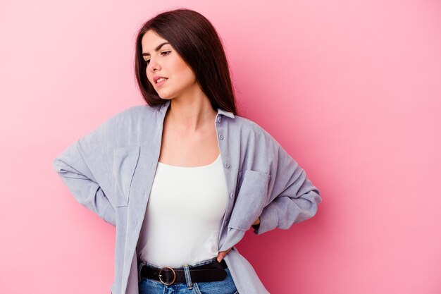 Young caucasian woman isolated on pink wall suffering a back pain.