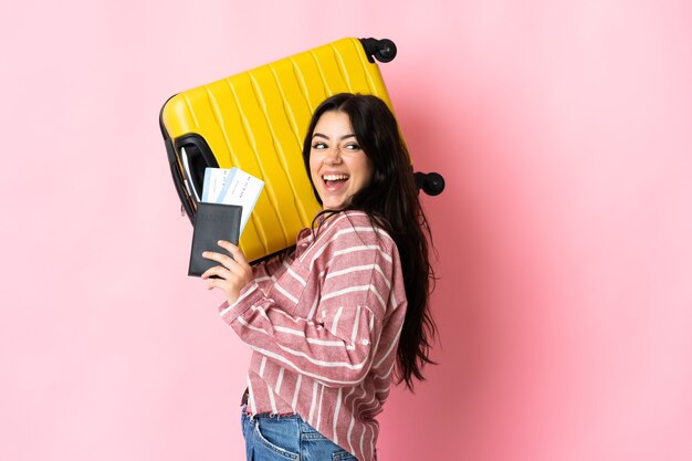 Young caucasian woman isolated on pink wall in vacation with suitcase and passport