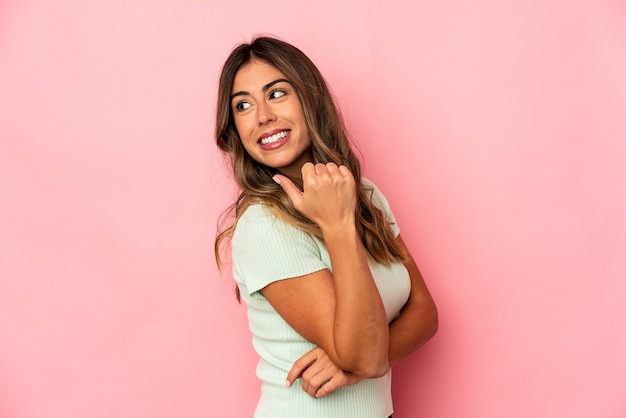 Young caucasian woman isolated points with thumb finger away, laughing and carefree.