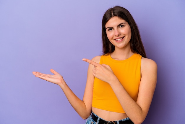 Young caucasian woman isolated on purple background excited holding a copy space on palm.