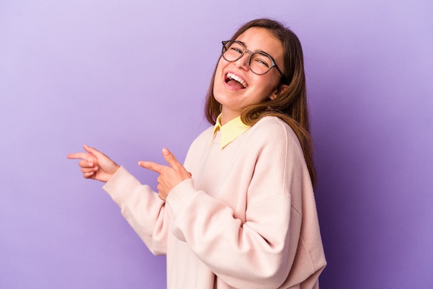 Young caucasian woman isolated on purple background excited pointing with forefingers away.