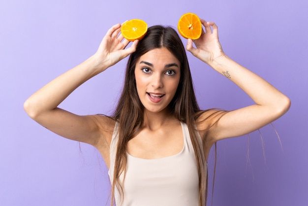 Young caucasian woman isolated on purple background holding an orange