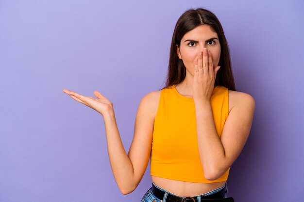 Young caucasian woman isolated on purple background impressed holding copy space on palm