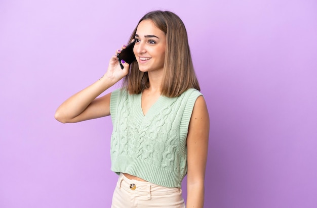 Young caucasian woman isolated on purple background keeping a conversation with the mobile phone