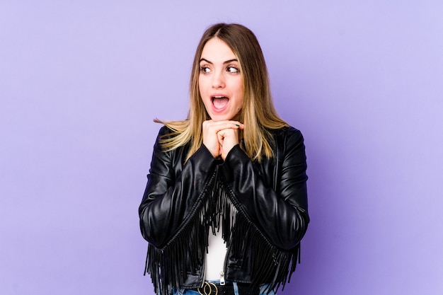 Young caucasian woman isolated on purple background praying for luck, amazed and opening mouth looking to front.