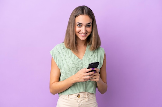 Young caucasian woman isolated on purple background sending a message with the mobile