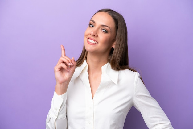 紫色の背景に分離された若い白人女性は、最高の兆候を示して指を持ち上げます