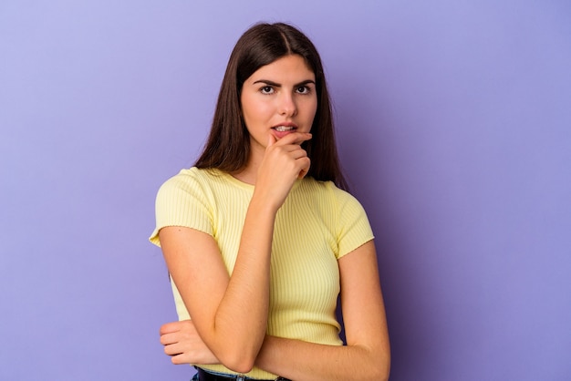 Young caucasian woman isolated on purple background suspicious, uncertain, examining you.